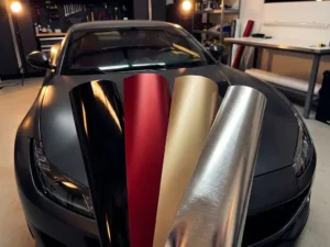 Sportwagen met uitgewaaierde vinyl wrap stalen in zwart, mat rood, champagnegoud en chroom op de motorkap in professionele werkplaats.