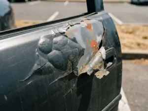 Loszittende en bladderende vinylwrap op autodeurpaneel, met verkleurde lak eronder zichtbaar in fel middagzonlicht.