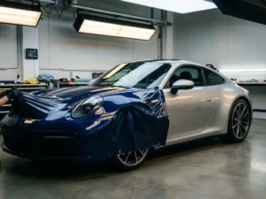Sportwagen half ingepakt in midnight blue vinylwrap die wordt afgestript om het originele zilveren lakwerk te onthullen, in professionele workshop.