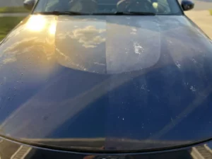 Sportswagenkap half bedekt met beschermende vinylfolie, met zichtbaar contrast tussen levendige blauwe lak en vervaagde zonbeschadigde verf.