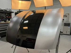 Sportwagenpaneel met drie vinylwrap afwerkingen naast elkaar: matte houtskool, glanzend zwart en satijn zilver, belicht in professionele workshop.