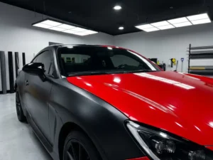 Sportwagen met gesplitst carwrap design, matte zwarte en glanzende rode vinylfolie op de carrosserie, gefotografeerd in professionele wrapstudio.