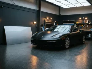 Sportauto met matte zwarte vinylwrap naast origineel zilver lak paneel in professionele wrapstudio met epoxyvloer.