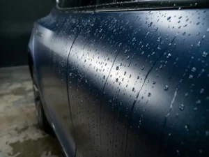 Waterdruppels parelend op een glanzend metallic blauwe vinylwrap van een autoportierdeel, close-up met dieptescherpte.