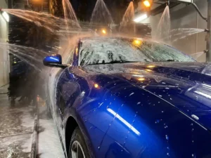 Glanzend metallic blauw vinyl-gewrapte auto in carwastunnel met waterparels en schuim op het perfecte oppervlak.