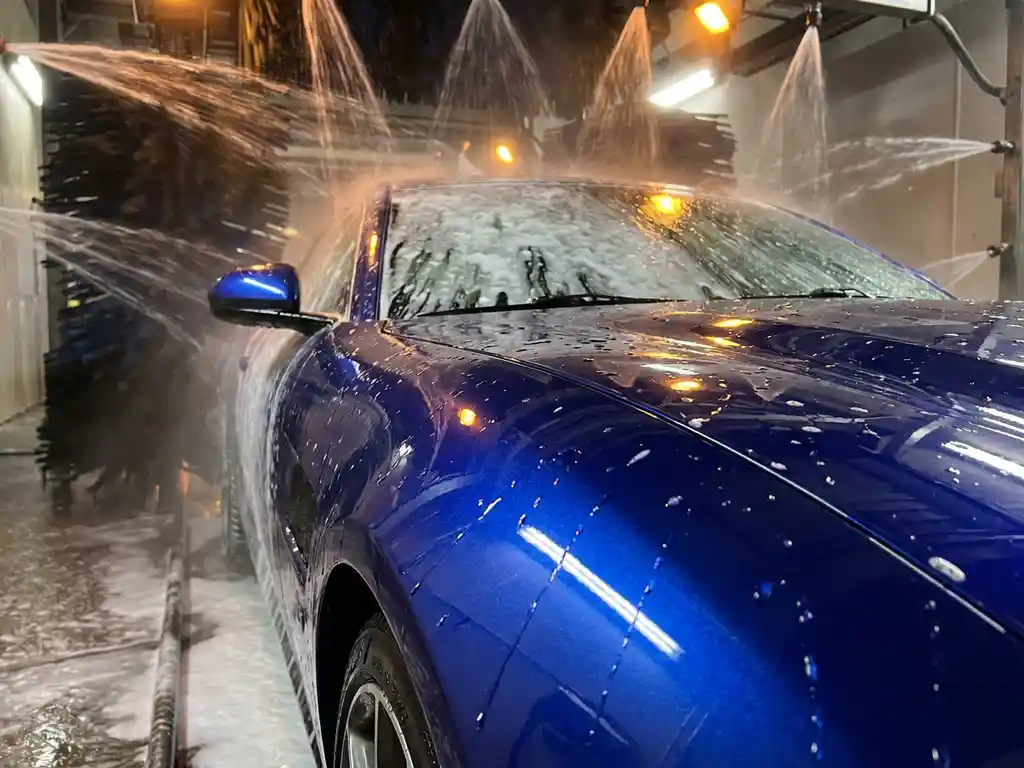 Glanzend metallic blauw vinyl-gewrapte auto in carwastunnel met waterparels en schuim op het perfecte oppervlak.