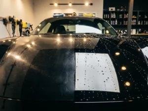 Luxe sportwagenhood half mat met wervelkrassen, half spiegelglad met keramische coating en waterdruppels, in professionele detaillingsstudio.