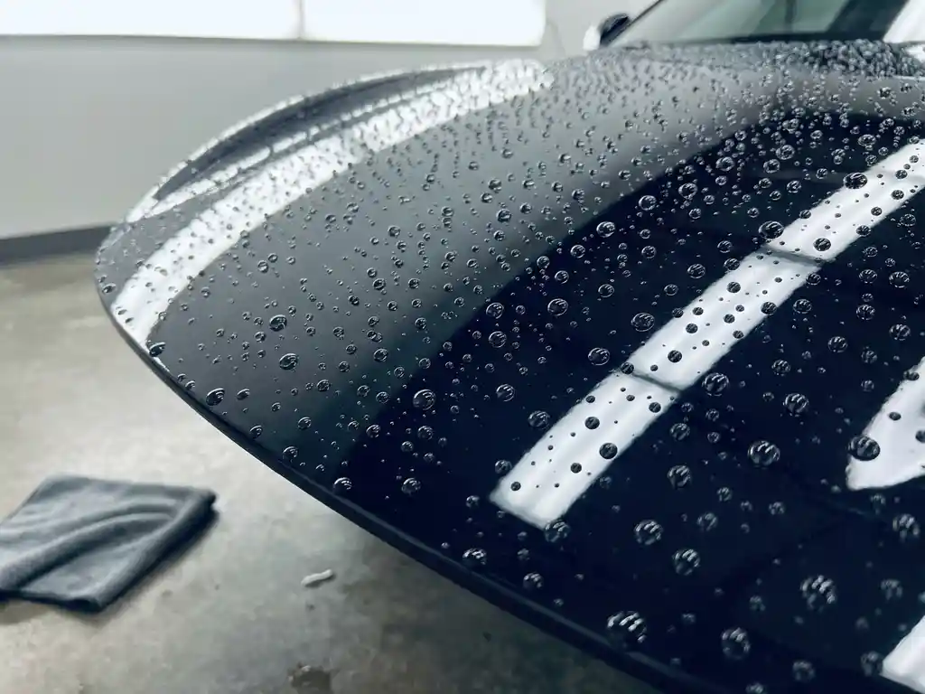 Glanzende zwarte sportwagen met keramische coating waarop waterdruppels parelend afhouden, microvezel doek op gepolijste betonvloer.