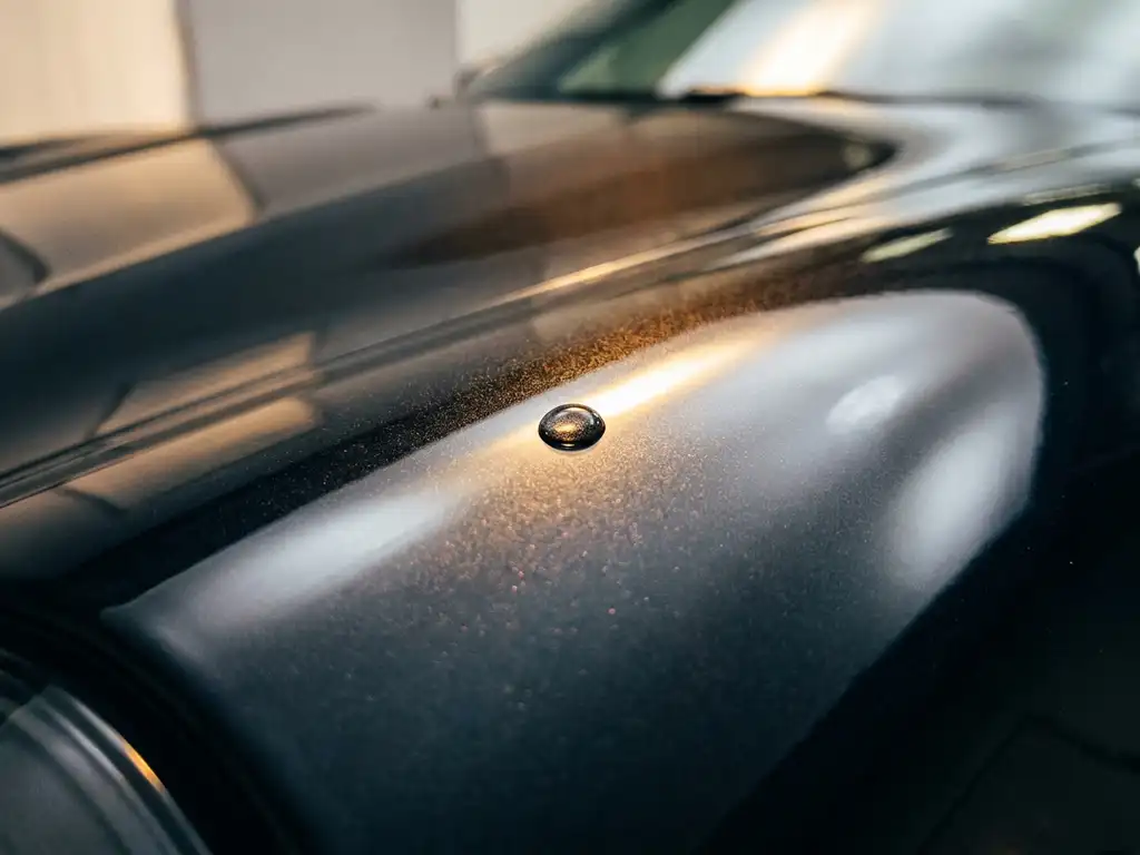 Keramisch gecoat sportwagenkoetswerk met perfecte waterdruppel op diepzwarte metallic lak, gouden studiolicht.