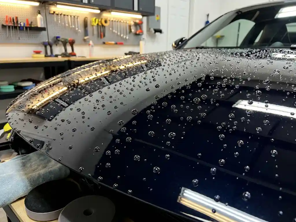 Glanzende zwarte motorkap met keramische coating en parelachtige waterdruppels in professionele detailing studio.