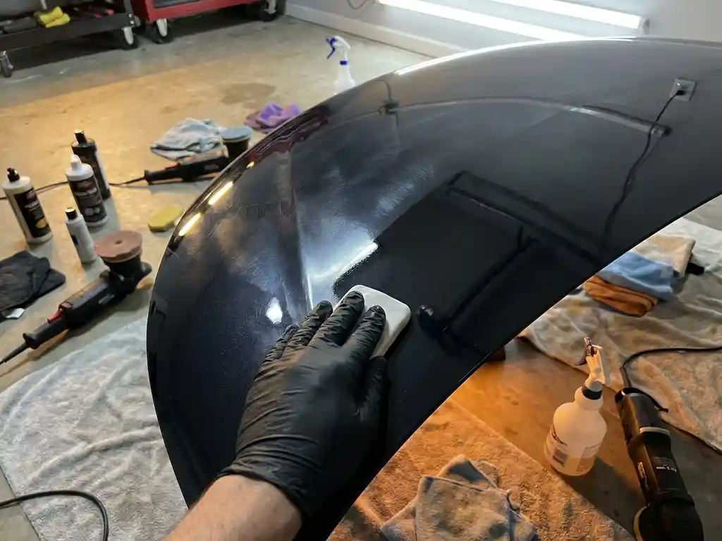 Detailer die met witte kleibar zwart metallic autolak bewerkt tijdens paint correction, omringd door polijstgereedschap en microvezeldoeken.