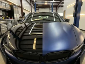 Sportauto met glanzende zwarte PPF op de ene helft en matte middernachtblauwe wrap op de andere, gefotografeerd in een professionele werkplaats.